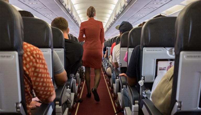 Female cabin crew walks away down aircraft cabin isle